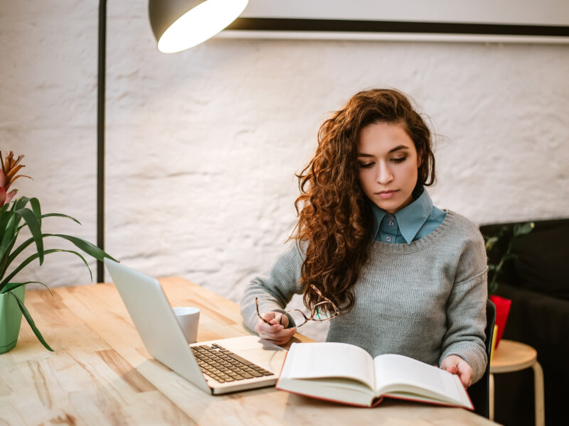 Woman reading book while sitting by the desk.